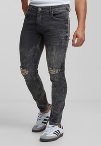Fekete farmernadrág, slim fit szabásban, kopott térdrész foltokkal, fakult mosással, fémből készült gombos zárással és klasszikus ötpocket dizájnnal.