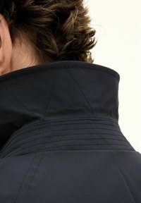 Navyblaue Jacke mit sichtbarem Stich, strukturiertem Stoff, schräger Kragenform und glatter Oberfläche. Nahaufnahme des Rückens.