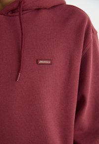Maroon hoodie made of soft fabric, featuring a drawstring hood and a stitched Dickies logo label on the front.