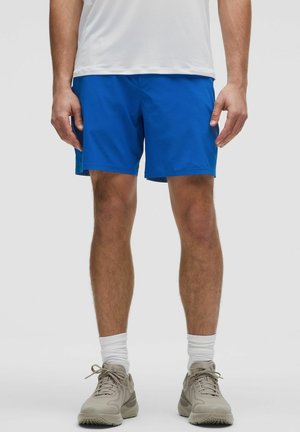 Pantaloni sportivi blu realizzati in un tessuto leggero, con cintura elastica e taglio a metà coscia. Abbinati a scarpe grigie e calze bianche.