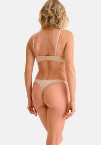 Ensemble de lingerie beige comprenant un soutien-gorge et un string. Tissu lisse, bretelles ajustables et fermeture à crochets au dos avec un design minimaliste.