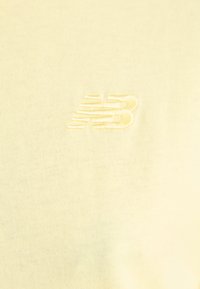 T-shirt jaune clair en coton avec une texture douce, arborant un logo "NB" brodé dans une teinte légèrement plus foncée de jaune.