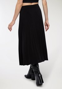 Gonna midi plissettata nera con una fascia larga in vita e tessuto morbido, abbinata a stivali neri con tacco a blocco fino al ginocchio.