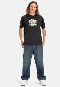 Sort kortærmet t-shirt med et grafisk design af blomster og stjerner. Bæres med løse blå denimjeans og hvide sneakers.