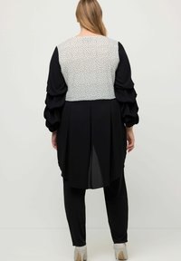 Conjunto negro con un respaldo texturizado con un patrón blanco, mangas largas con volantes y una silueta fluida. Incluye un detalle de abertura en la parte posterior.