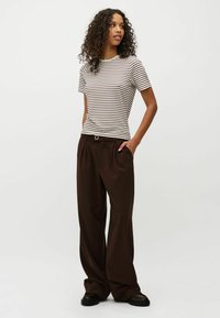 Top de manga corta a rayas en beige y marrón, combinado con pantalones marrones de corte holgado, con pliegues delanteros y pierna ancha.