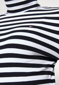 Black and white striped turtleneck sweater made of ribbed fabric, featuring a small logo accent on the left chest area.