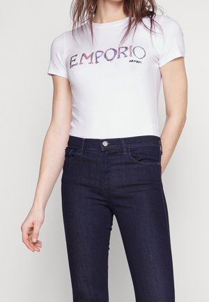 T-shirt blanc à manches courtes avec le logo "EMPORIO ARMANI" en lettres colorées, associé à un jean denim foncé avec une coupe classique et des poches.