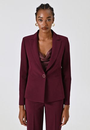 Blazer bordeaux dal design sartorial con rever a punta, chiusura con un solo bottone e spalle strutturate. Finitura in tessuto liscia.