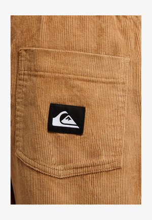 Hnědá kapsa z kordurové tkaniny s černo-bílou nášivkou s logem Quiksilver přišitou uprostřed kapsy.