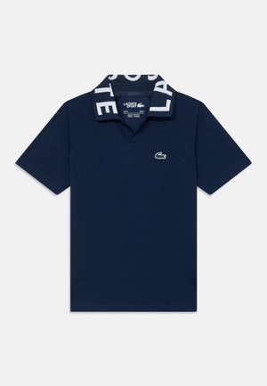 Pólo azul-marinho feito de algodão, com uma gola de padrão contrastante que apresenta a letra "LACOSTE" e um pequeno logótipo de crocodilo verde no peito.