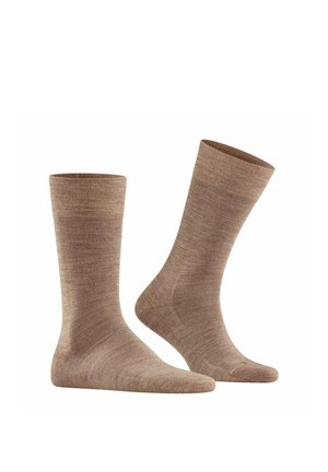 Paar braune Wollsocken bis zur Mitte der Wade, eines aufrecht stehend und das andere schräg, als ob getragen, auf weißem Hintergrund.