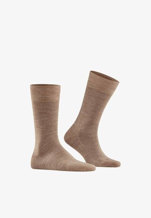 Paar braune Wollsocken bis zur Mitte der Wade, eines aufrecht stehend und das andere schräg, als ob getragen, auf weißem Hintergrund.