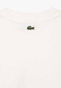T-shirt blanc col rond avec un petit logo crocodile vert brodé centré sous le col arrière.