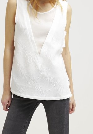 White textured top with a deep V-neck, layered over a sheer panel. The fabric has a subtle pattern, complemented by relaxed, sleeveless design.