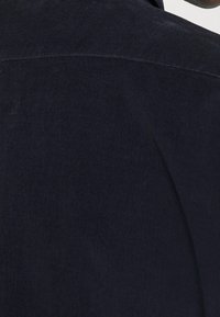 Tissu en velours côtelé bleu marine avec des rayures verticales ; vue en gros plan montrant la texture et les détails du tissu, avec un design de col lisse.
