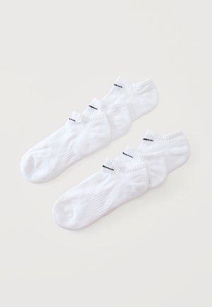 Dwa komplety po trzy pary białych skarpetek do kostki z małym czarnym ściegiem na mankiecie, ułożone płasko na jasnej powierzchni.