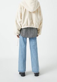 Chaqueta cropped de pelo sintético color crema con capucha, combinada con una camisa de tejido en blanco y negro y jeans de pierna ancha de color azul claro. Botas de plataforma negras.