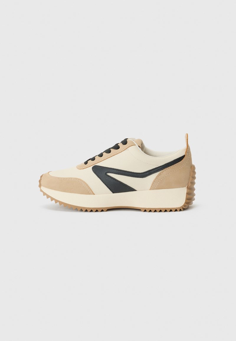 Baskets beige et crème avec des accents noirs, en suède et cuir, semelle en caoutchouc texturée et design classique à lacets.