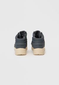 Para ciemnoszarych wysokich sneakersów Skechers z jasnobeżowymi podeszwami, widzianych z tyłu na tle białego tła.
