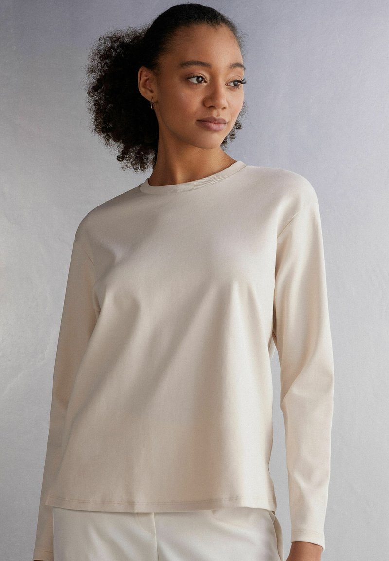 Beige Langarmhemd aus Baumwolle mit rundem Ausschnitt, glatter Textur und lässiger Passform, das ein minimalistisches Design ohne sichtbare Muster aufweist.