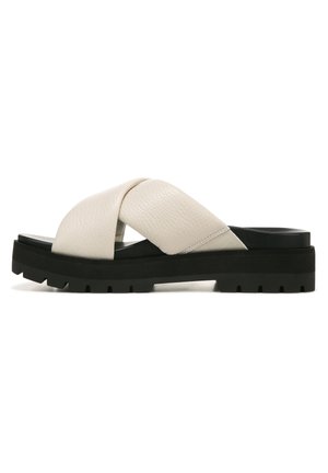 Leather slide sandal with a cross-strap design, light beige color, thick black rubber sole, and textured accents for added grip.
