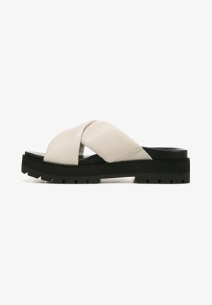 Leather slide sandal with a cross-strap design, light beige color, thick black rubber sole, and textured accents for added grip.