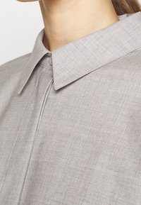 Hellgraues Hemd mit einem Kentkragen, subtil strukturiertem Stoff und einer Vorderseite mit einer linearen Nahtdetails.