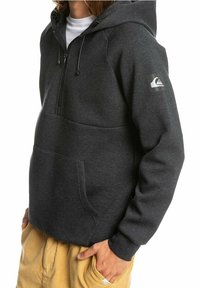 Harmaa collegehuppari pehmeästä kankaasta, jossa on etutasku, säädettävä nyörillinen huppu ja logo vasemmassa hihassa.