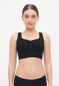 Top sportivo nero con spalline larghe, arricciature al centro testurizzate e design senza cuciture. Abbinato a pantaloni corti neri a vita alta coordinati.