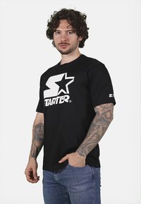T-shirt in cotone nero con un grande logo bianco "Starter" e una grafica a stella sul davanti. Maniche corte e scollo a girocollo.