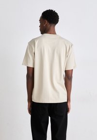 Beige bomull t-skjorte med avslappet passform og korte ermer. Har rund hals og minimal sømdetalj bak.