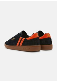 Sneaker nere in suede con strisce arancioni, suola in gomma e dettagli in logo dorato. Design low-top con punta arrotondata e colletto imbottito.