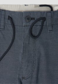 Gros plan sur un pantalon à carreaux bleu marine et blanc avec fermeture à boutons et cordon noir passé dans les passants de ceinture.