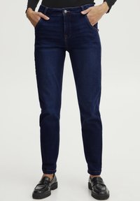 Temno modri jeans s sproščenim krojem, z sprednjimi žepi, gumbom za zapiranje in kontrastnim šivanjem. Gladka tekstura brez vzorcev.