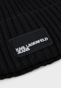 Bonnet en tricot noir à côtes avec un revers. Présente une étiquette noire rectangulaire avec "KARL LAGERFELD JEANS" brodé en blanc.