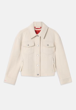 Veste blanche courte en tissu doux, avec un col pointu, des boutons argentés, deux poches à l'avant et une doublure intérieure rouge.