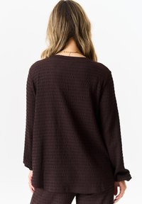 Brown textured long-sleeve top with a loose fit. Features a crew neckline and dropped shoulders, displayed from the back.