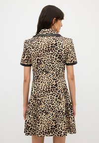 Abito a fantasia leopardata con maniche corte, colletto nero e rifiniture, gonna svasata e texture morbida; che mette in evidenza un audace motivo animale.