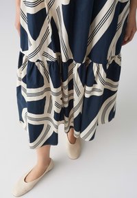 Flowy navy and cream patterned dress with tiered ruffles; features geometric designs and soft fabric. Model wears light-colored flats.