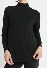 Pull noir à col roulé avec manches longues, fabriqué en tissu doux et texturé. Présente une coupe décontractée et des poignets côtelés.