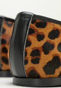Botte en imprimé léopard avec une finition en cuir noir et une texture lisse. Présente des bords arrondis et une semelle plate. Coutures visibles en accent.
