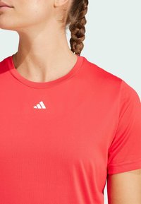 Red athletic t-shirt with a round neckline, short sleeves, made of smooth fabric. Features a white logo on the upper left.