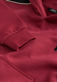 Bordeaux hoodie met een voorzak en geribde manchetten. Zachte stof met een gestructureerde afwerking en een contrasterende zwarte binnenhood.