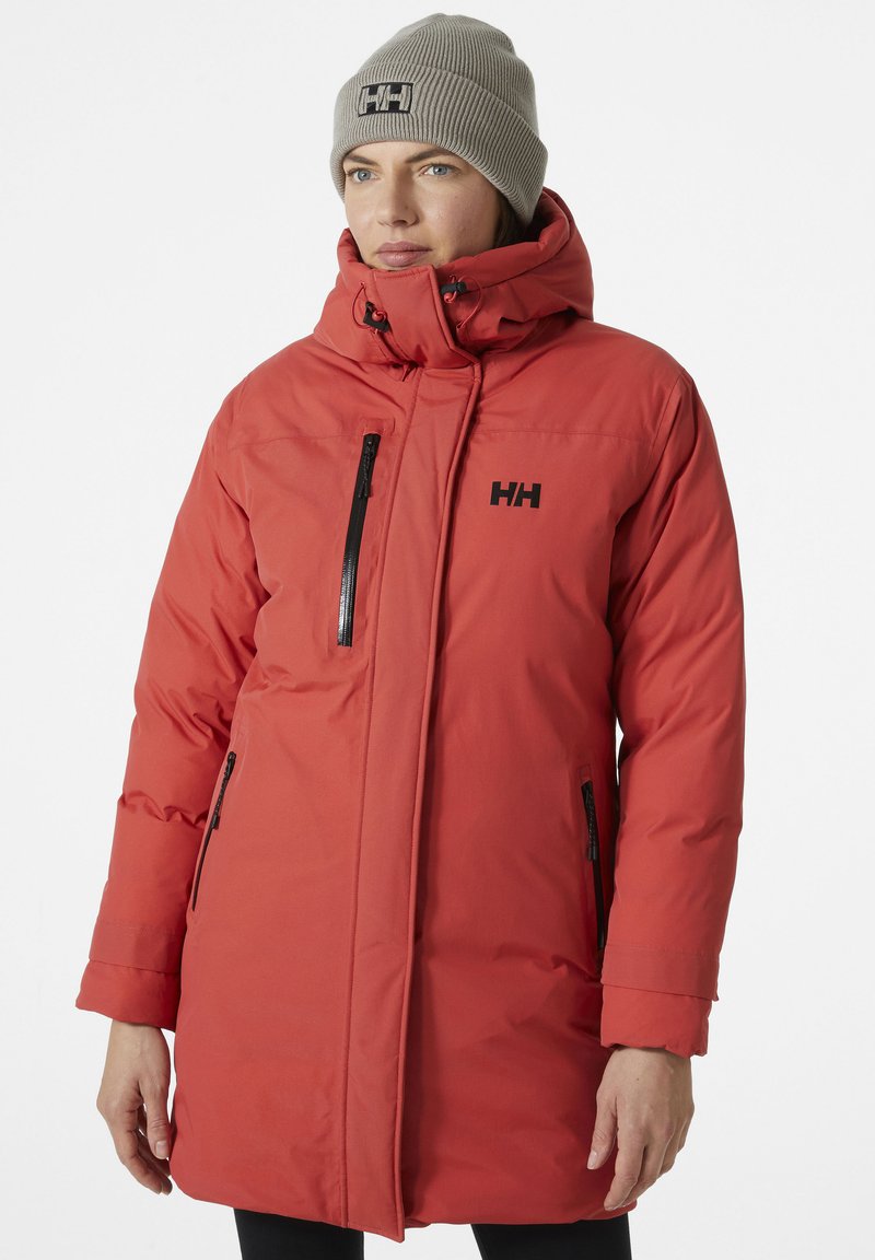 Chaqueta de plumas roja con un alto cuello, bolsillos con cremallera y marca en negro. El material es suave y las mangas tienen un ligero puño.