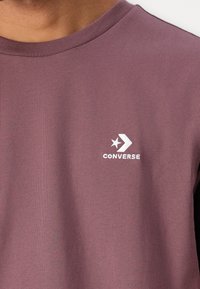 Bordo bombažna majica s krojem okoli vratu. Bele vezenine zlog "Converse" in detajlom z zvezdo ter puščico na prednjem delu.