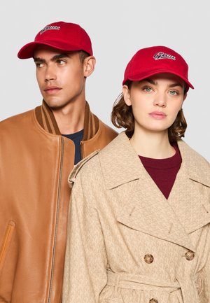 Cappello rosso con logo ricamato, materiale in cotone. Giacca bomber in pelle color cuoio con colletto a coste. Trench beige con texture a motivo e bottoni.