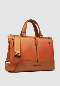 Oranje leren en stoffen tas met dubbele handvatten, verstelbare riem, ritssluiting aan de voorkant en een textuur aan de onderkant. Voorzien van een logodetail.