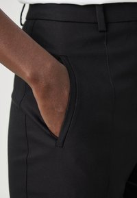 Svarta byxor i ett slätt, strukturerat tyg, med en ficka på sidan och en figurnära design som betonar en elegant silhuett.