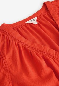 Rode linnen blouse met een V-hals, geplooide textuur en gestikte schouderdetails. Etiket zichtbaar bij de hals.